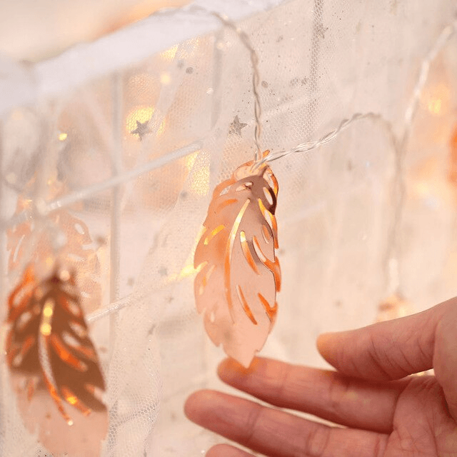 close up of someone touching a rose gold feather fairy light